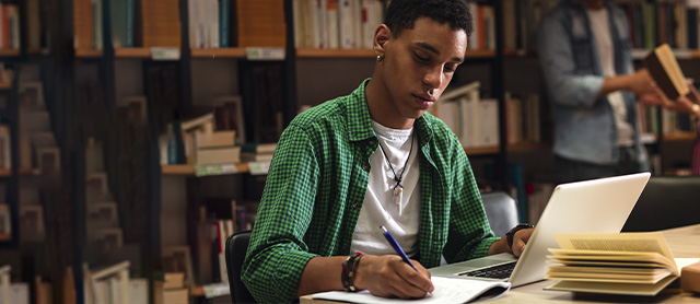 rapaz estudando em uma biblioteca e fazendo anotações em um caderno