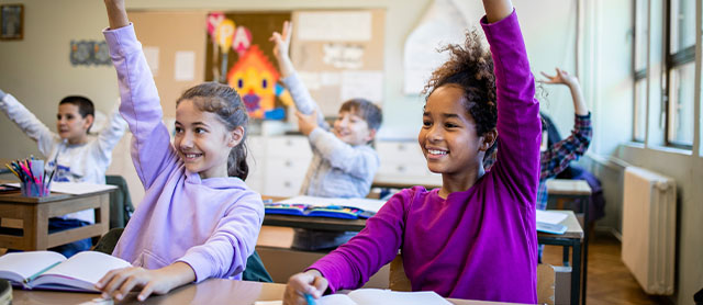 crianças do ensino fundamental na sala de aula levantando as mãos