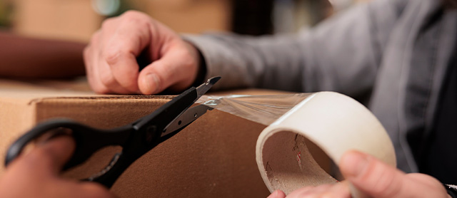mulher usando fita adesiva para lacrar uma caixa de papelão